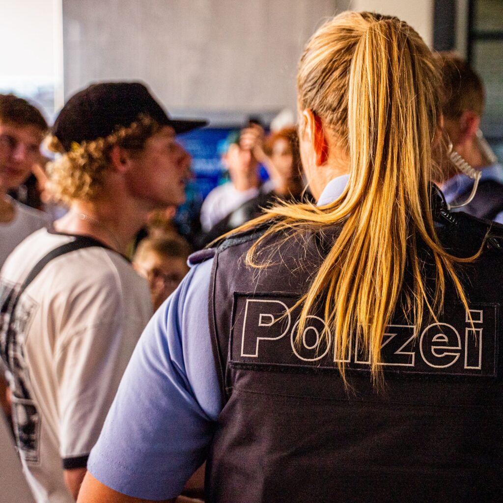 A policewoman interacts with a group of young people indoors, providing security and assistance.